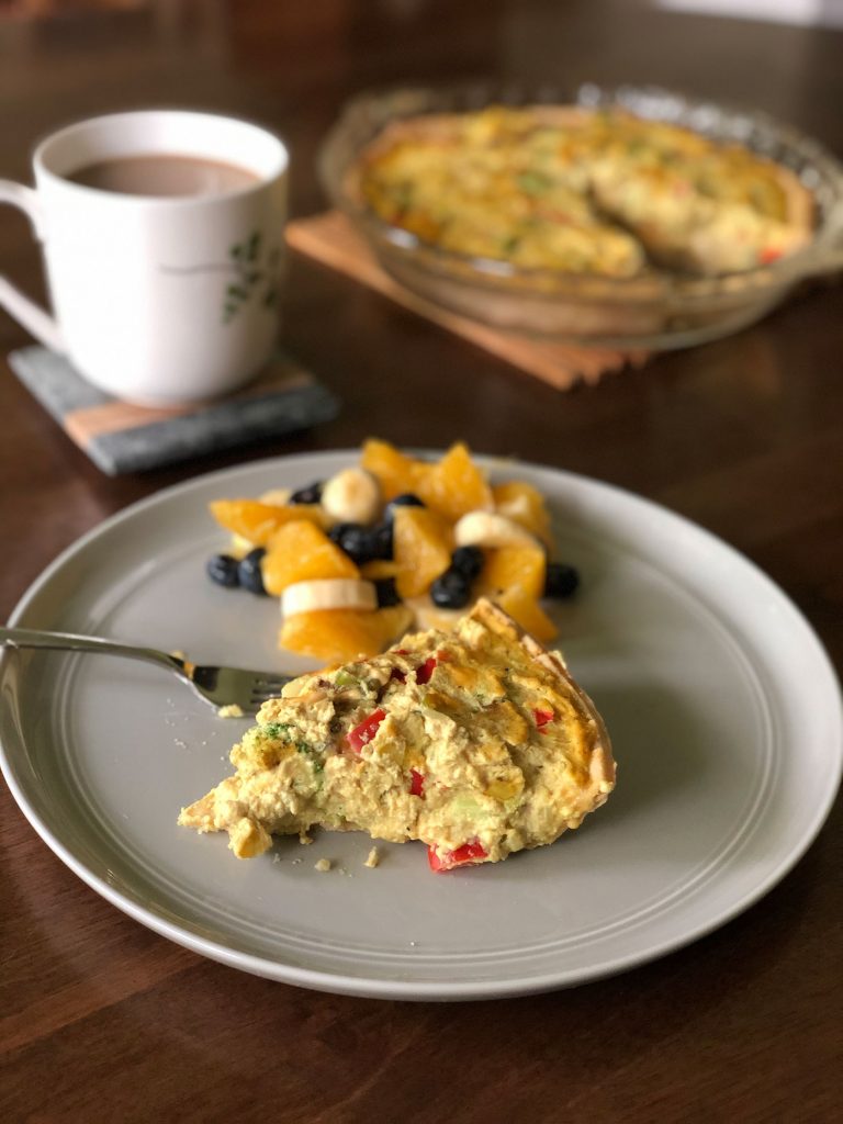 Slice of tofu vegetable quiche with a side of fruit and coffee