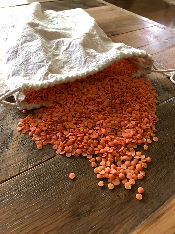 red lentils in a canvas reuseable bag poured onto a wood table